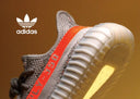 Zapatilla deportiva Adidas gris y naranja con parte superior de tejido texturizado y suela acanalada.
