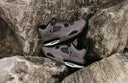 Un par de zapatillas Air Jordan 4 grises y negras con suelas blancas.